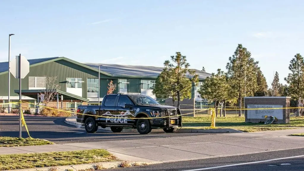 A police vehicle is parked in front of a school building with yellow caution tape around it, indicating a restricted or secured area.
