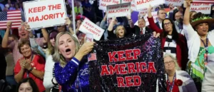 A crowd celebrates with signs and a sequined banner that reads "Keep America Red."