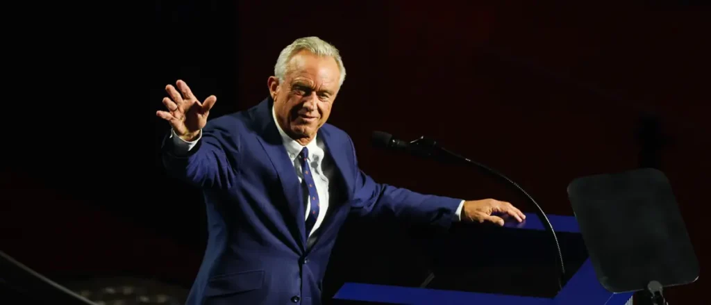 A man in a suit gestures with his hand while standing at a podium, likely delivering a speech or presentation.