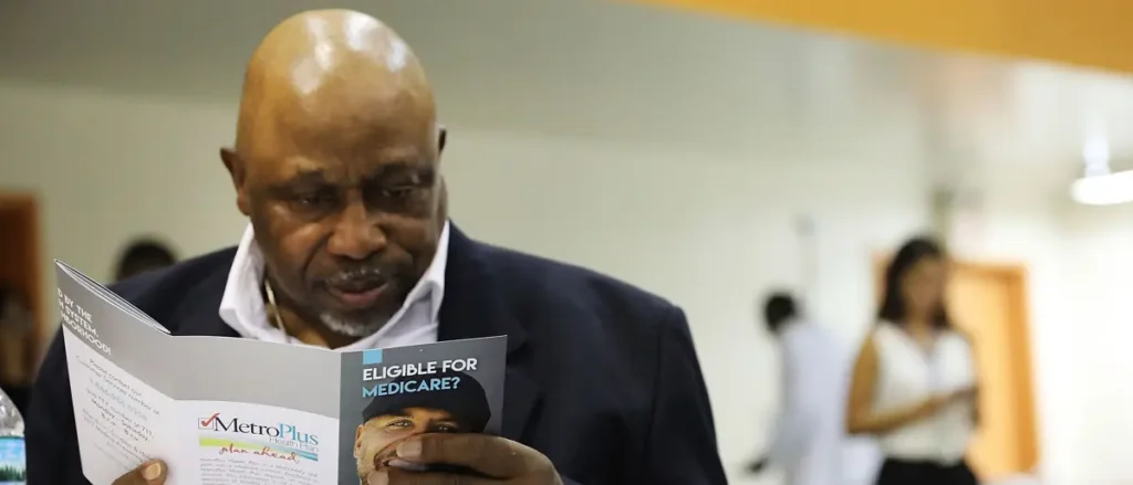 A man is reading a brochure titled "Eligible for Medicare?" at what appears to be a community event or informational session.