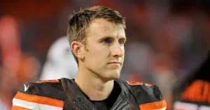 The image shows a football player in a black and orange uniform, looking off to the side with a focused expression.