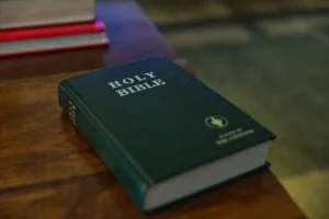 The image shows a close-up of a green Holy Bible placed on a wooden surface, with a blurred background.