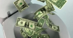 The image depicts a toilet with one-dollar bills falling into it, symbolizing the waste of money.