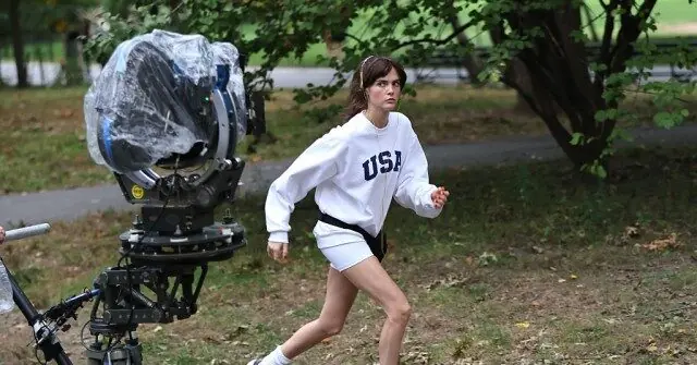 A person in a white "USA" sweatshirt is running in a park, with a camera rig in the foreground.