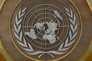 The image shows the emblem of the United Nations, featuring a world map surrounded by laurel branches.