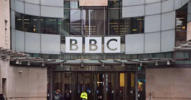 The image shows the exterior of a BBC building with the BBC logo prominently displayed on the facade.