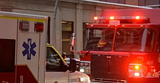 An ambulance and a fire truck are parked in front of a building with their lights on, indicating an emergency response.