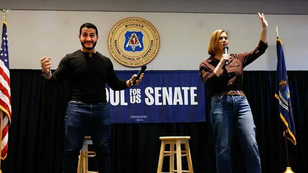 Two individuals are on stage at a campaign event for the U.S. Senate, with one holding a microphone and the other gesturing.