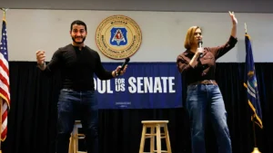 Two individuals are on stage at a campaign event for the U.S. Senate, with one holding a microphone and the other gesturing.