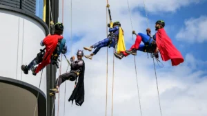 A group of people dressed as superheroes rappel down the side of a tall building.