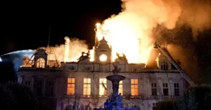 A historic building is engulfed in flames and smoke at night, with firefighters attempting to extinguish the blaze.