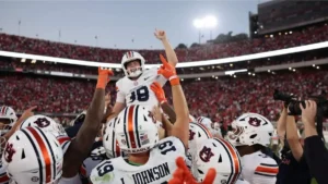 Auburn football players celebrate a victory with their teammates in a stadium filled with fans.