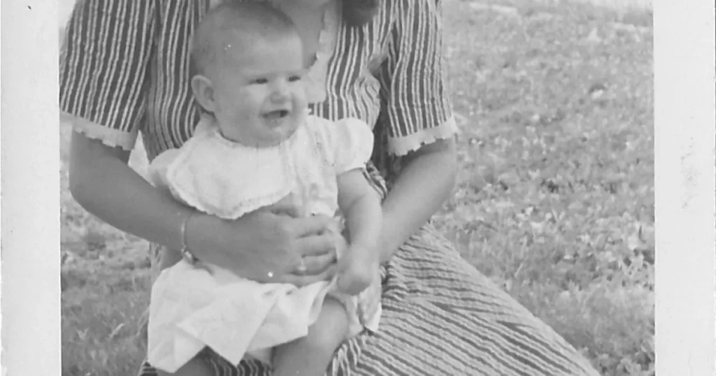 A joyful baby smiles while being held by someone in a striped dress outdoors.