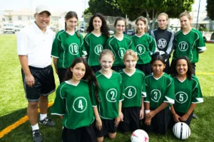 A youth soccer team poses for a group photo with their coach on a sunny day.