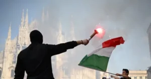 A person waves an Italian flag and holds a flare in front of the iconic Milan Cathedral.