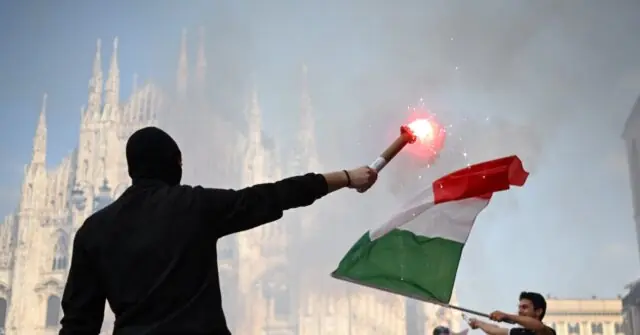 A person waves an Italian flag and holds a flare in front of the iconic Milan Cathedral.