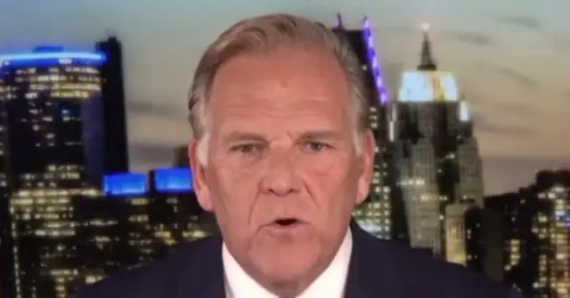 The image shows a news anchor in a studio with a cityscape background, likely representing a major urban area.
