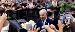 A man in a suit is surrounded by a crowd of people taking photos and videos with their phones.