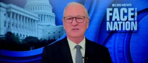 The image shows a news anchor on the set of CBS News' "Face the Nation," with the Capitol building in the background.