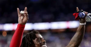 A football player celebrates with his hands raised, holding a towel and a small object, in a stadium setting.