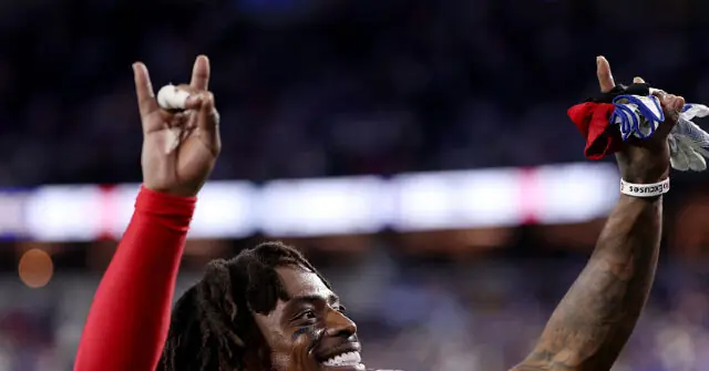 A football player celebrates with his hands raised, holding a towel and a small object, in a stadium setting.