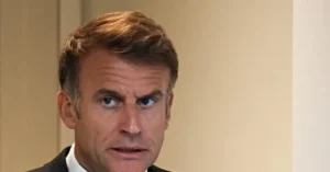 The image shows a man in a suit with a serious expression, likely during a news broadcast or interview.