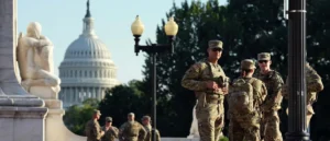 A group of soldiers in camouflage uniforms stands near a lamp post with the U.S. Capitol building in the background.