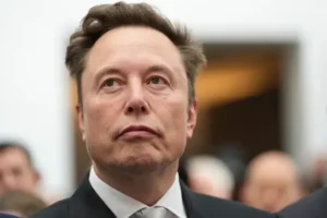 The image shows a man in a suit and tie, looking upwards with a serious expression.