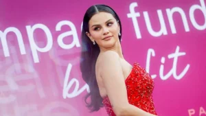 A woman in a red, beaded dress poses confidently in front of a pink backdrop with text.