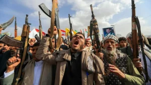 A group of individuals holds up weapons and appears to be shouting or chanting in a public gathering.