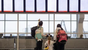 A family with backpacks and luggage stands in front of an airport departure board, checking their flight information.