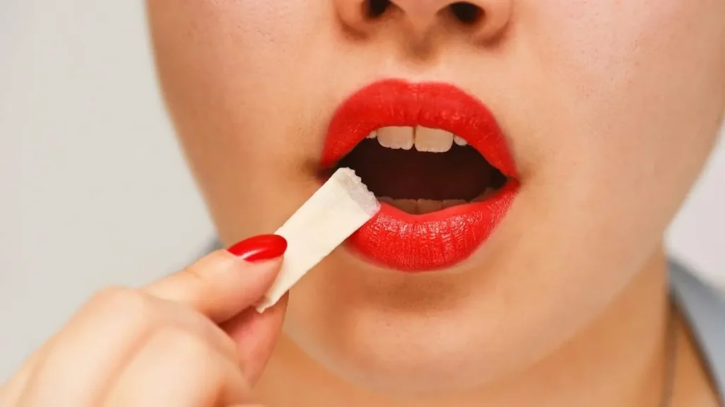 A person with red lipstick is holding a white object near their mouth.