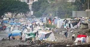 The image depicts a densely packed refugee camp with makeshift shelters and people engaged in various activities.