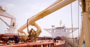 The image shows a large industrial setup with a pipeline system connected to a ship, likely involved in the transportation or processing of materials.