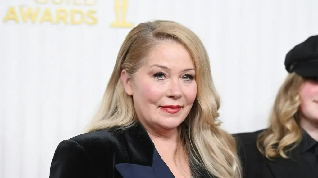 The image shows a person at the Golden Globe Awards, dressed in formal attire with a backdrop featuring the event's logo.
