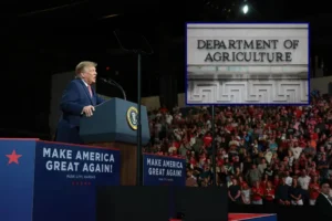 The image shows a political rally with a speaker at a podium and a crowd, alongside an inset of the Department of Agriculture building.