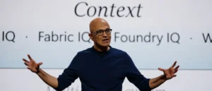 The image shows a person speaking on stage with a backdrop that includes the words "Context," "IQ," "Fabric IQ," "Foundry IQ," and "W."