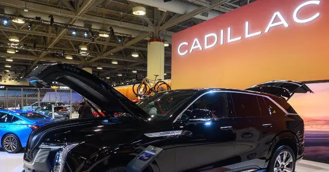 A Cadillac vehicle is displayed at an auto show with its hood and trunk open, showcasing its features.