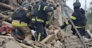 Rescue workers are seen searching through the rubble of a collapsed building, indicating a disaster response operation.