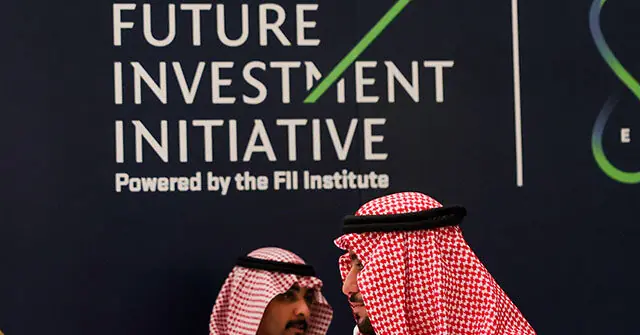 The image shows two individuals in traditional attire at the Future Investment Initiative event, powered by the FII Institute.
