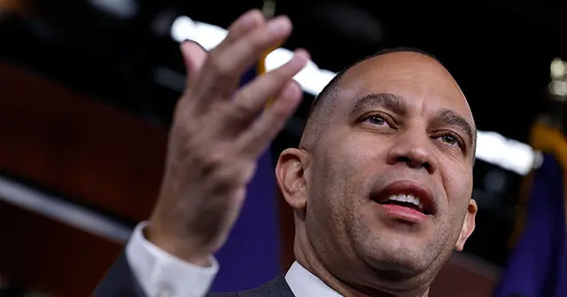 The image shows a man in a suit gesturing with his hand, appearing to speak or present in a formal setting.