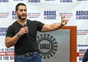 A man speaks at a podium with a UAW logo, addressing an audience at a campaign event for Abdul for US Senate.
