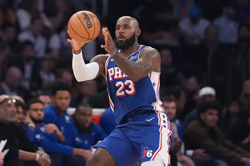 A basketball player in a Philadelphia 76ers uniform is seen dribbling the ball during a game.