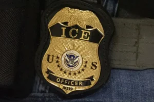 The image shows a close-up of a U.S. Immigration and Customs Enforcement (ICE) officer's badge.