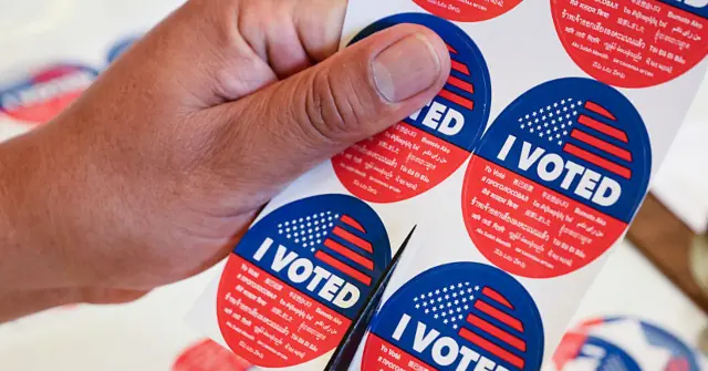 A hand is cutting an "I Voted" sticker from a sheet, symbolizing the act of voting.