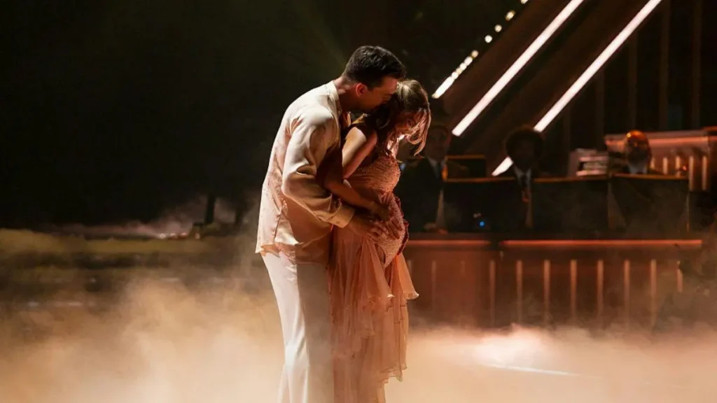 A couple shares an intimate moment on a stage with dramatic lighting and fog.