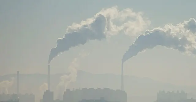 The image shows industrial smokestacks emitting thick plumes of smoke into the air, indicating significant air pollution.