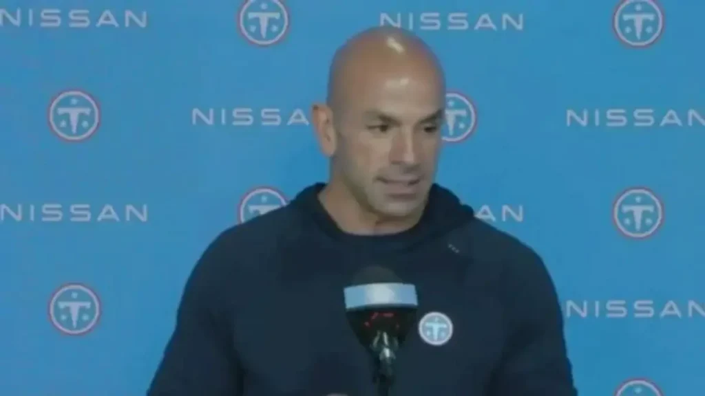 A man is speaking at a press conference in front of a backdrop featuring the Nissan logo.
