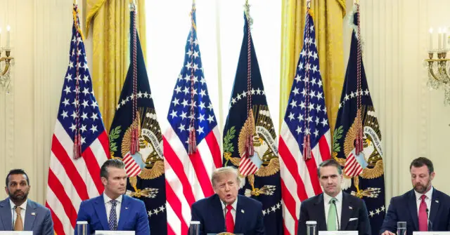 The image shows a formal press conference with several individuals seated at podiums in front of American flags and presidential seals.