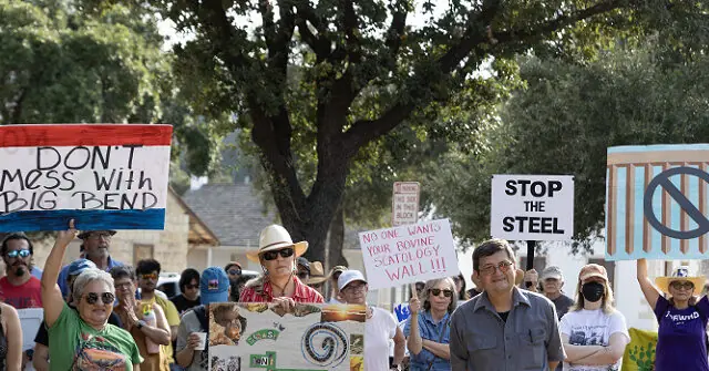 A group of people hold signs advocating against a proposed steel wall and protecting the environment in a protest.